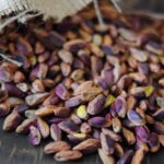 Ahşap bir masa üzerinde, ağzı açılmış bir çuvaldan dökülen bol miktarda kabuksuz, çiğ iç Antep fıstıklarının yakın çekim görüntüsü.